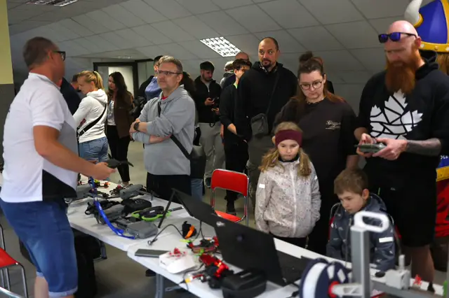 Stół z dronami, rodzice i dzieci przy warsztatach